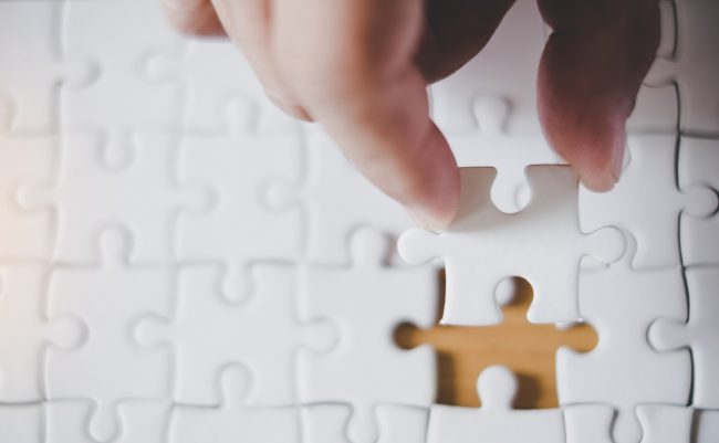 Hand holding piece of blank jigsaw puzzle with paper frame backg